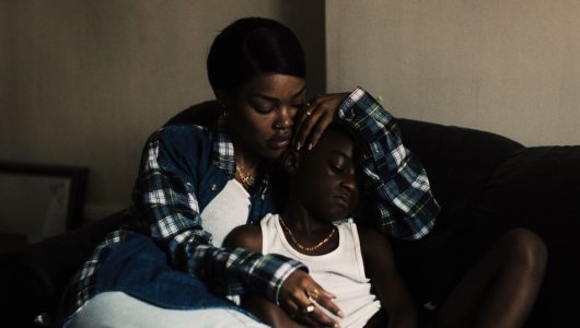 A Thousand and One_2023 Woman wraps boy in her arms on a couch.
